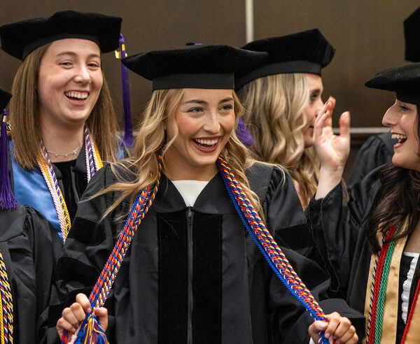Law student holding cords and smiling wearing cap and gown at graduation